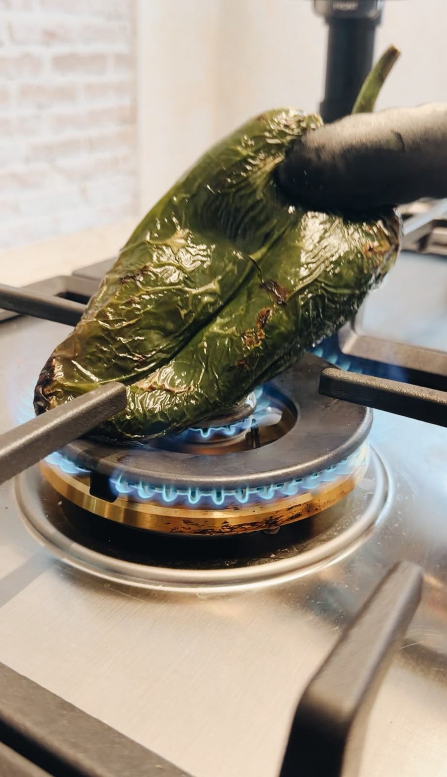 Chile poblano tatemándose directo sobre la flama azul de la estufa.