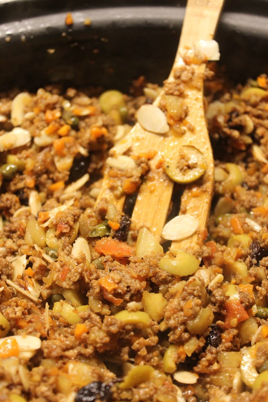 Cazuela de picadillo con fruta, aceituna, almendra y pasas, con cuchara de madera.