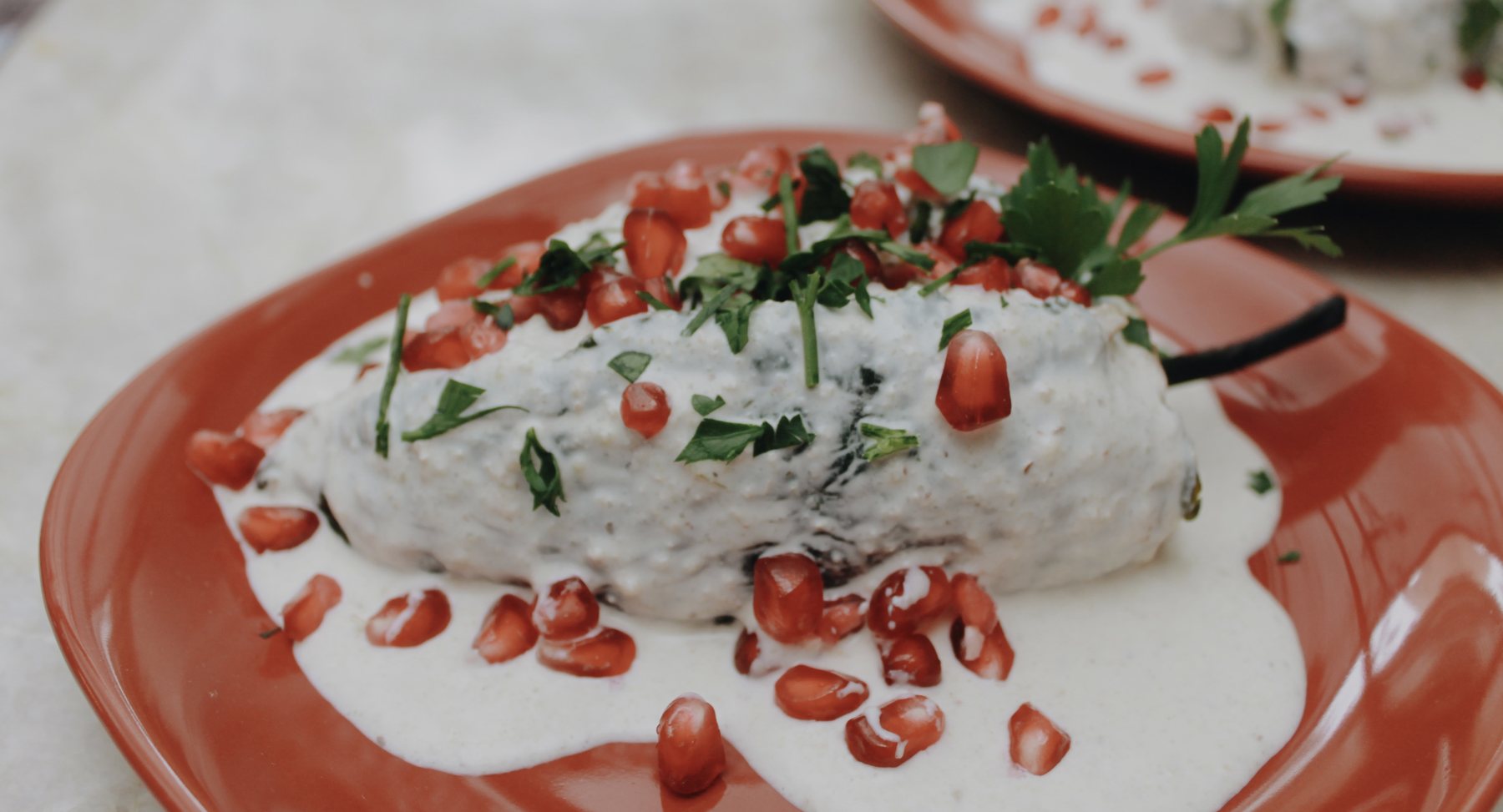 Chile en nogada de Patty Gourmet servido en plato de barro, bañado en nogada y coronado con granada y perejil.